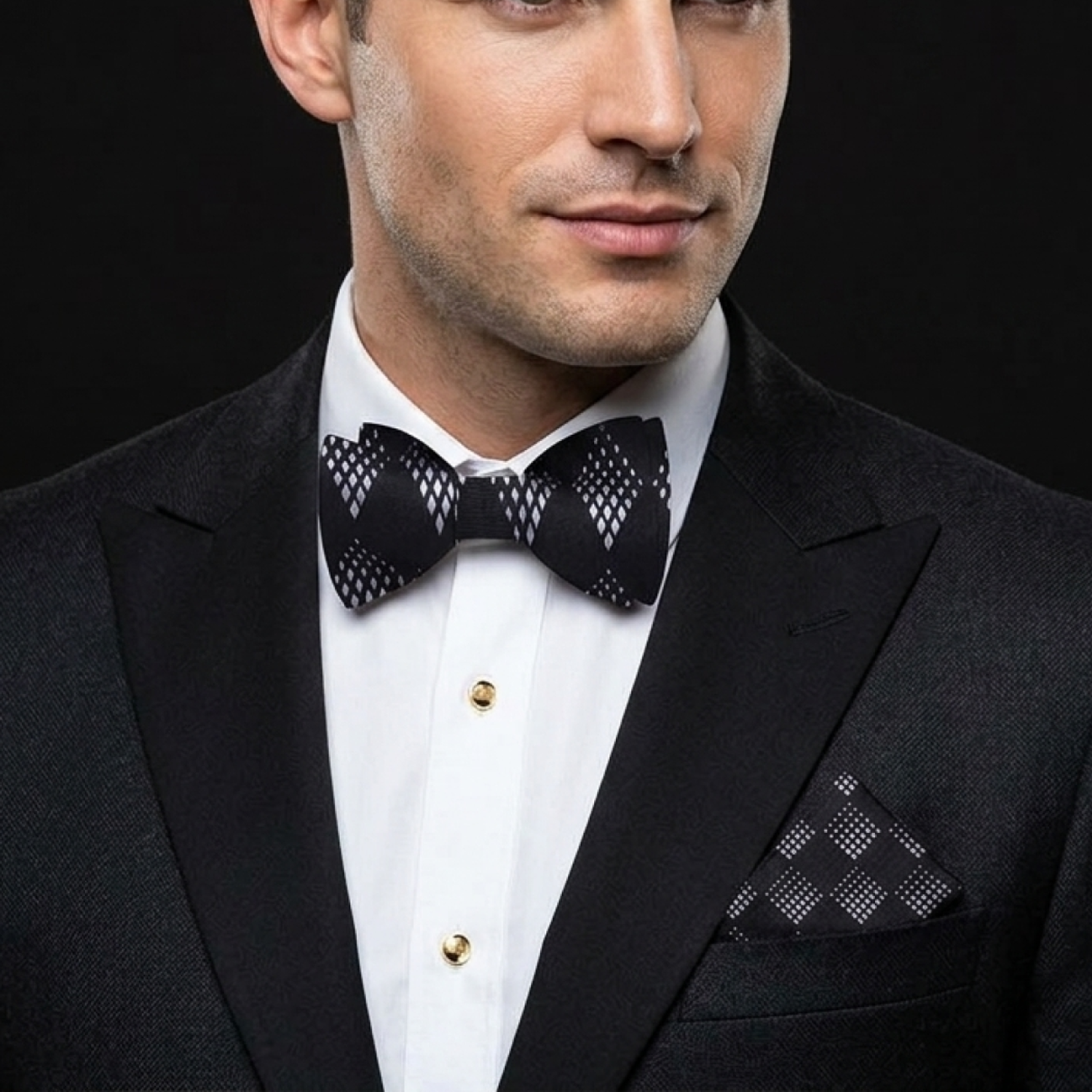 Man wearing a black tuxedo with a patterned bow tie and pocket square against a black background