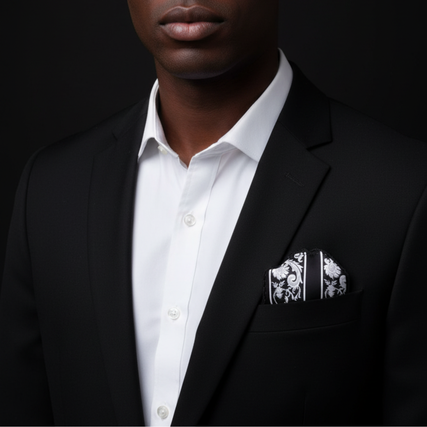 Man wearing a black suit with a white shirt and patterned pocket square against a dark background