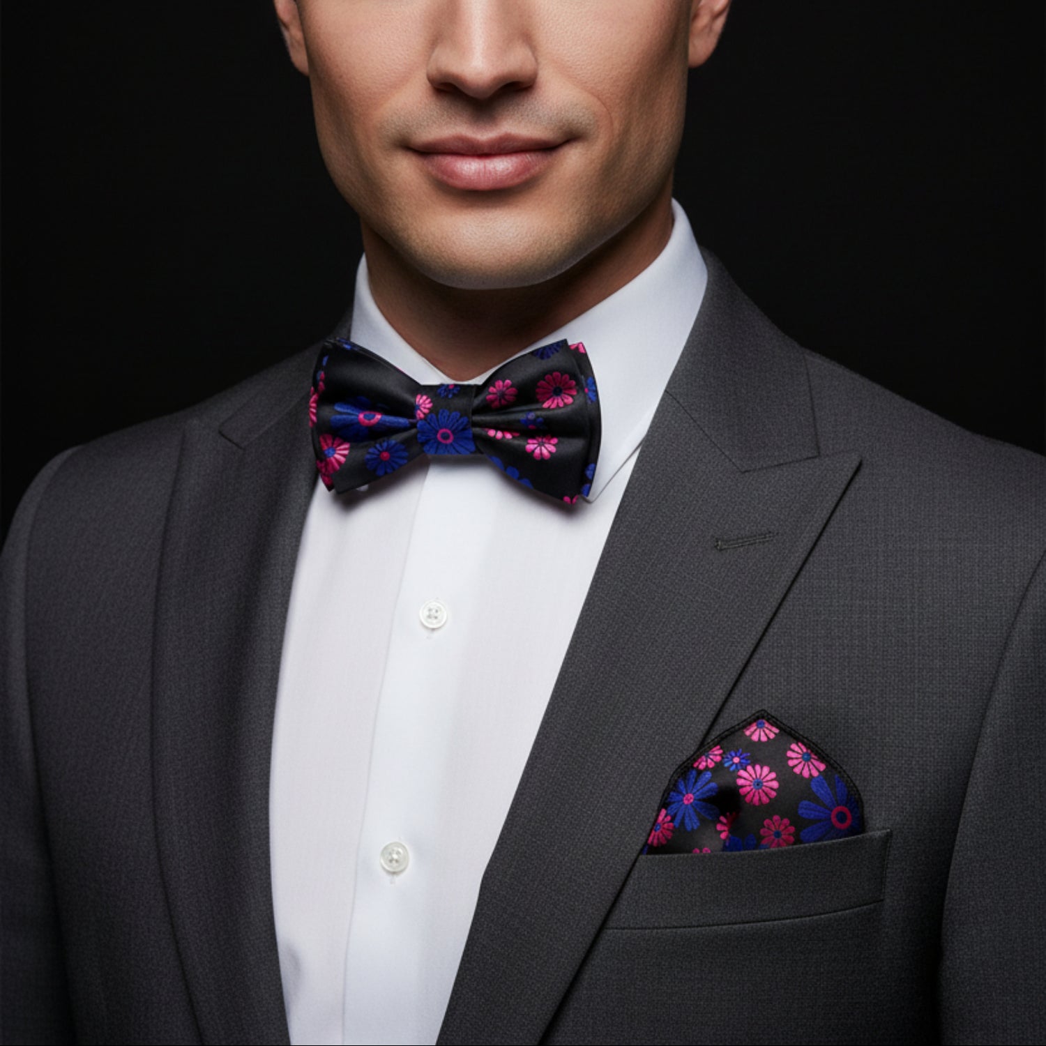 Man wearing a gray suit with a colorful bow tie and pocket square on a black background