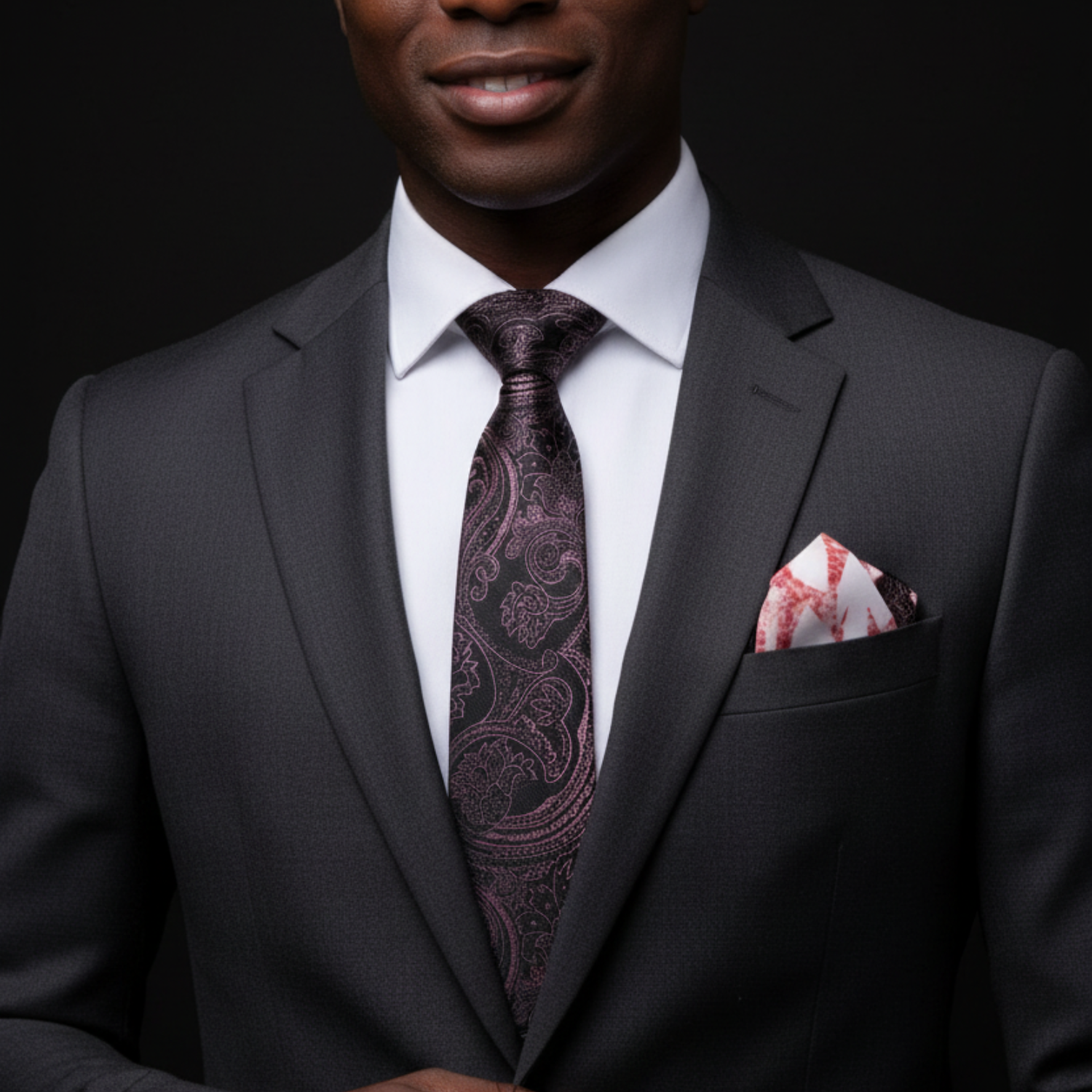 Man wearing a dark suit with a patterned tie and pocket square on a black background