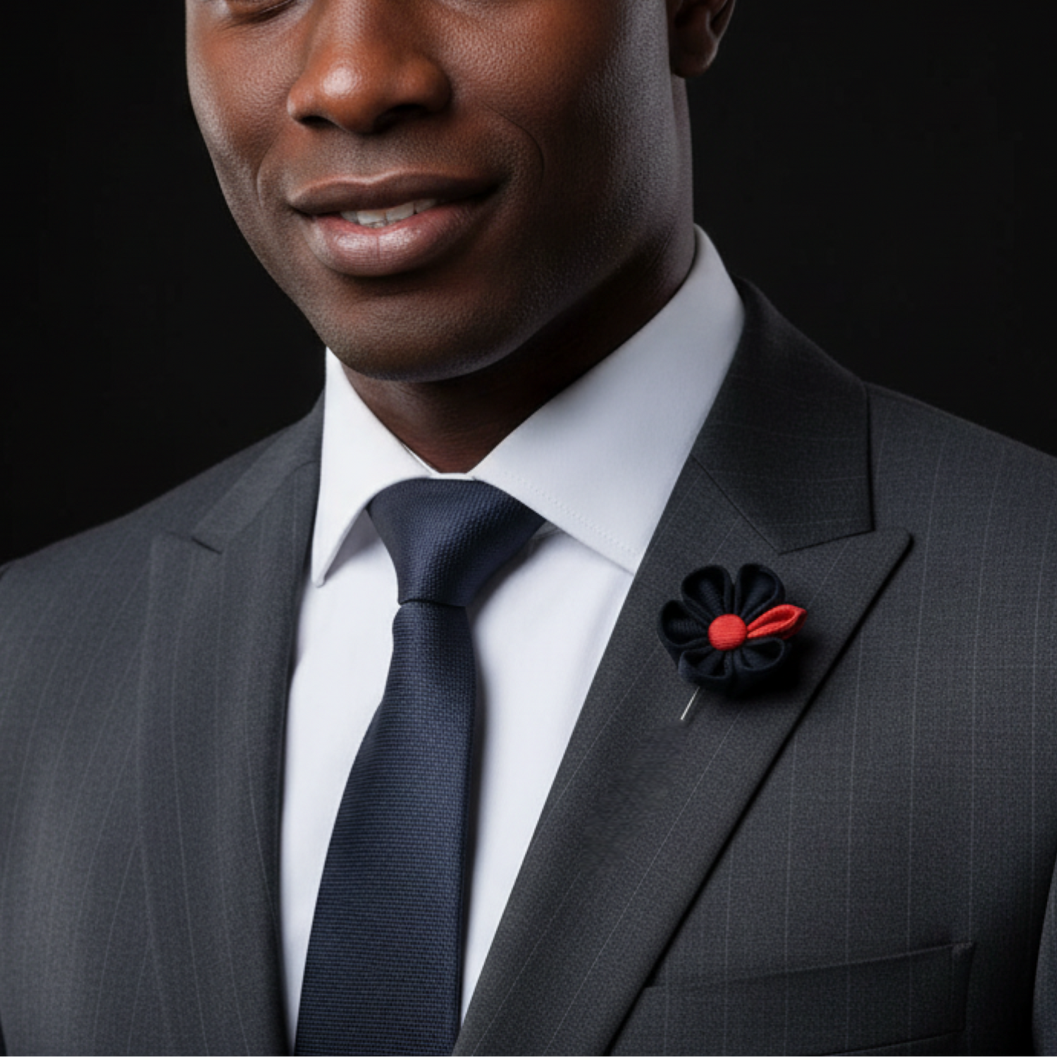 Man wearing a gray suit with a red and black flower pin on a black background