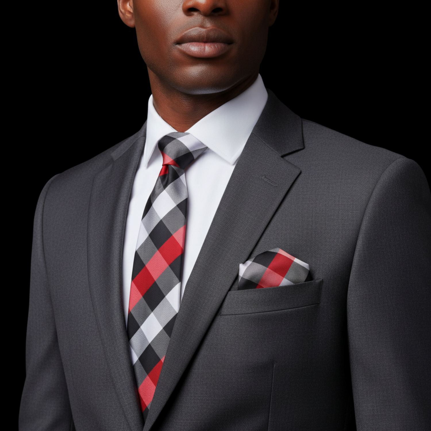 Man wearing a gray suit with a red and black checkered tie and pocket square on a black background