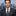 Man in a suit with a cityscape background wearing a black and silver tie and accenting grey square