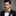 Man wearing a black suit with a red and blue checkered bow tie against a gray background