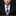 Man wearing a black suit with a white shirt and decorative tie on a dark background