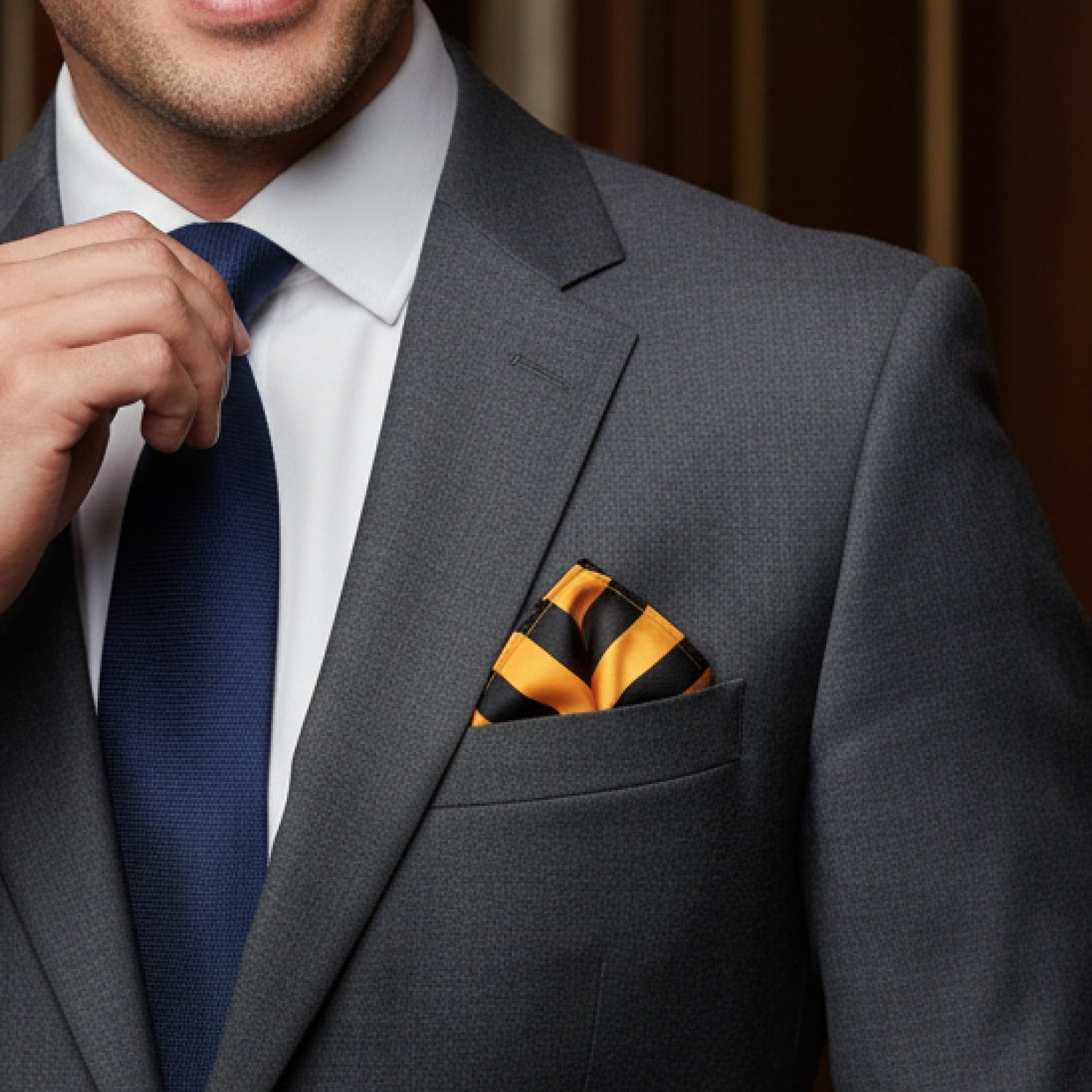 Man adjusting his blue tie with a gray suit and striped pocket square.