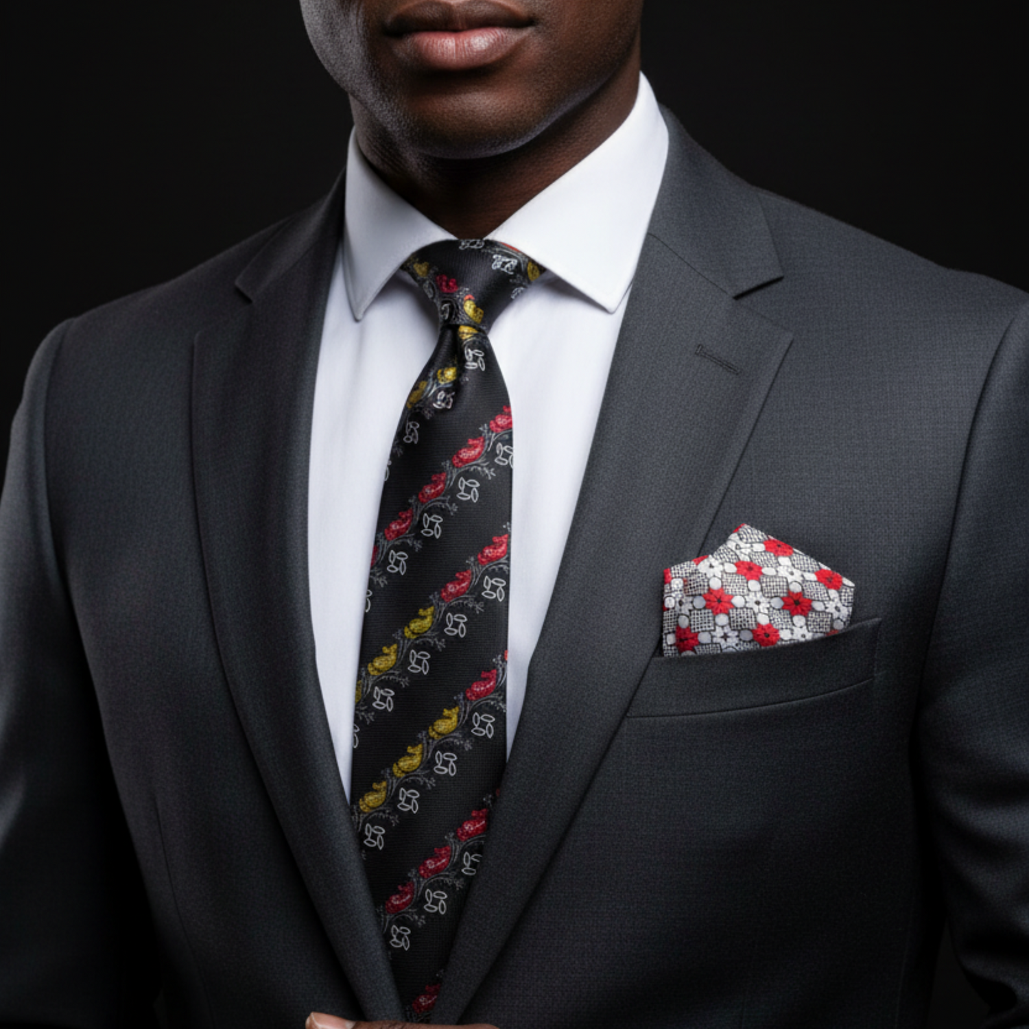 Man wearing a gray suit with a patterned tie and red, white, and blue pocket square on a black background