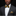 Man wearing a black suit with a yellow and black patterned bow tie and pocket square on a black background