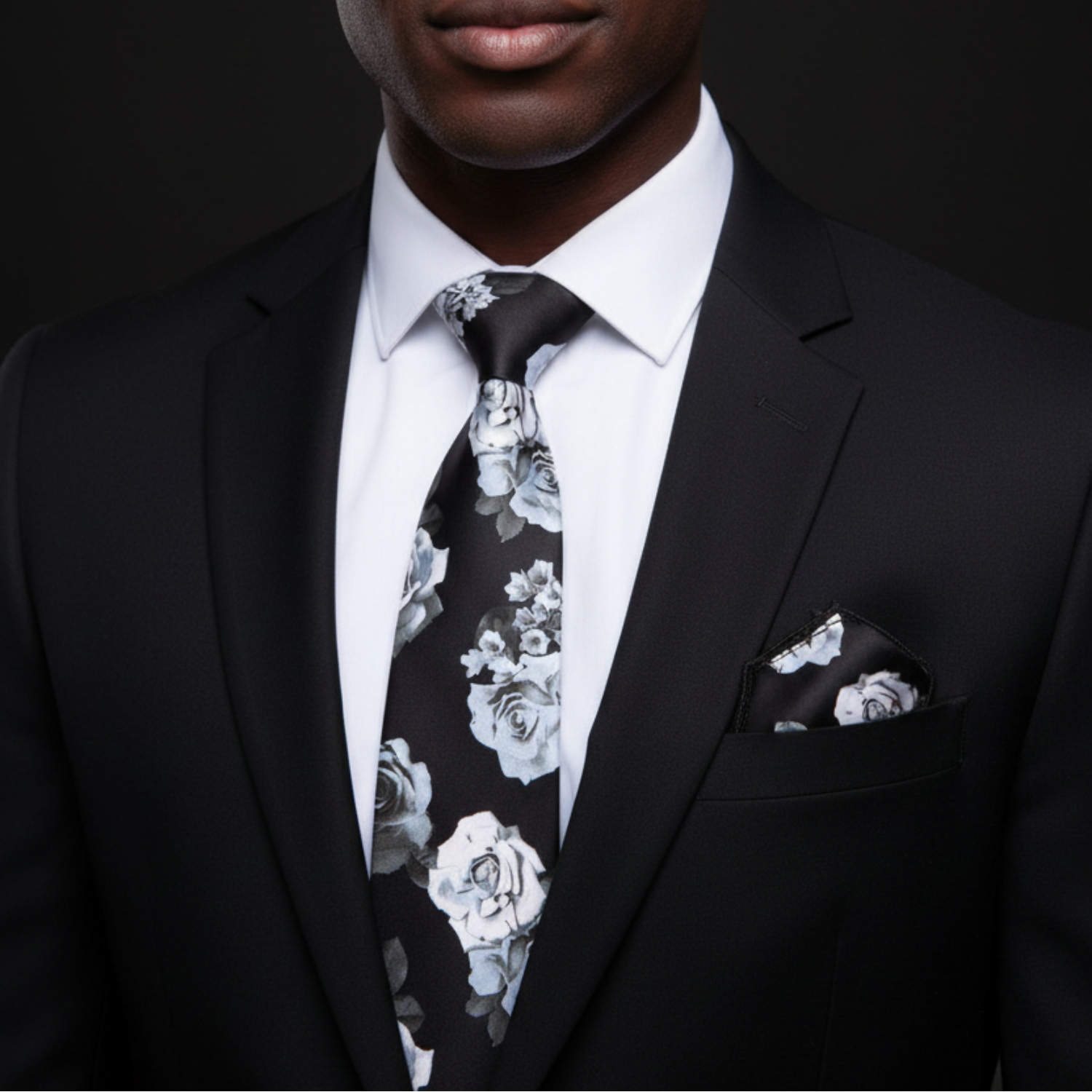 Man wearing a black suit with a floral tie and pocket square against a dark background