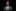 Man wearing a gray suit with a green tie and pocket square on a black background