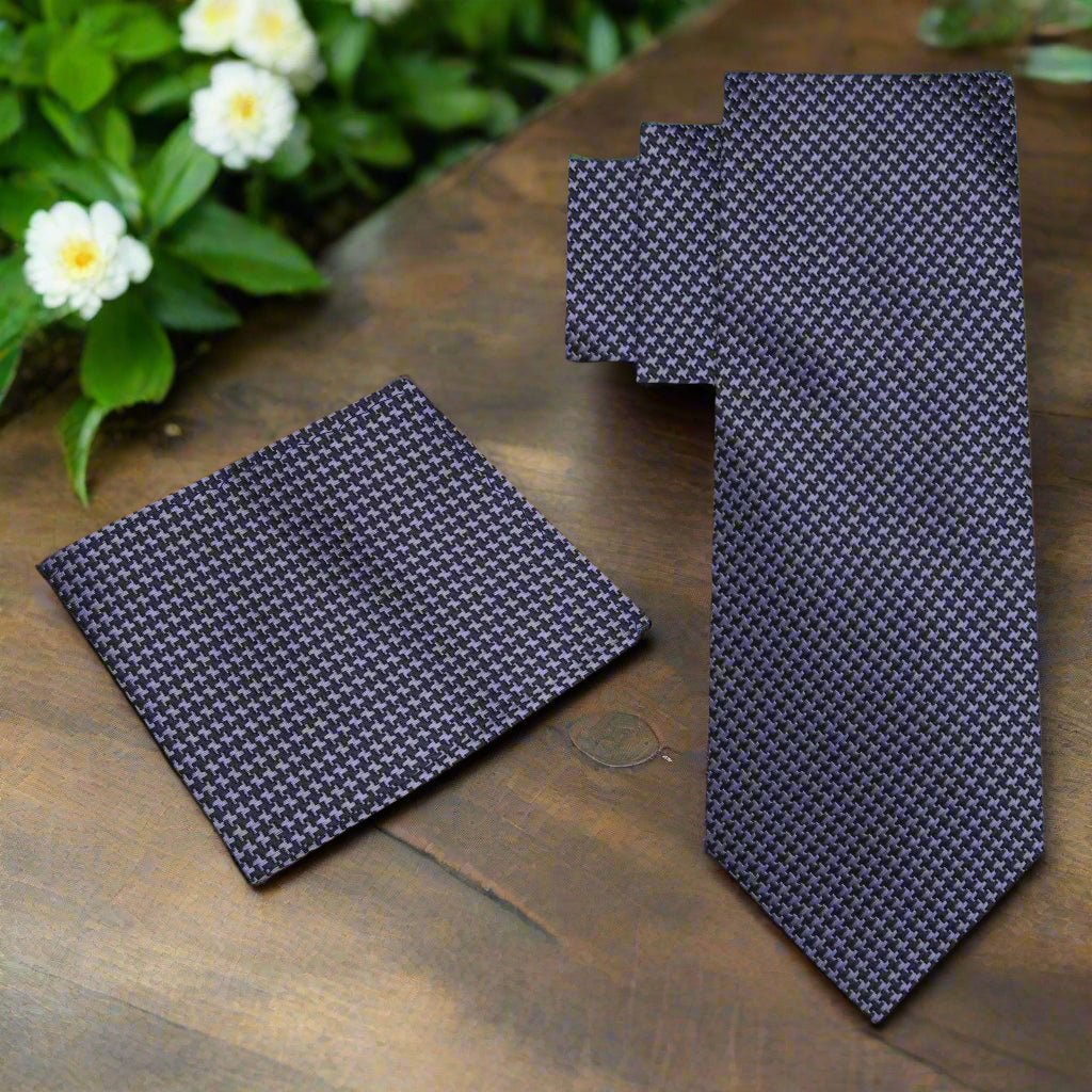 Navy patterned tie and pocket square on a wooden surface with greenery in the background