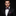 Man wearing a black suit with a purple bow tie and pocket square on a dark background