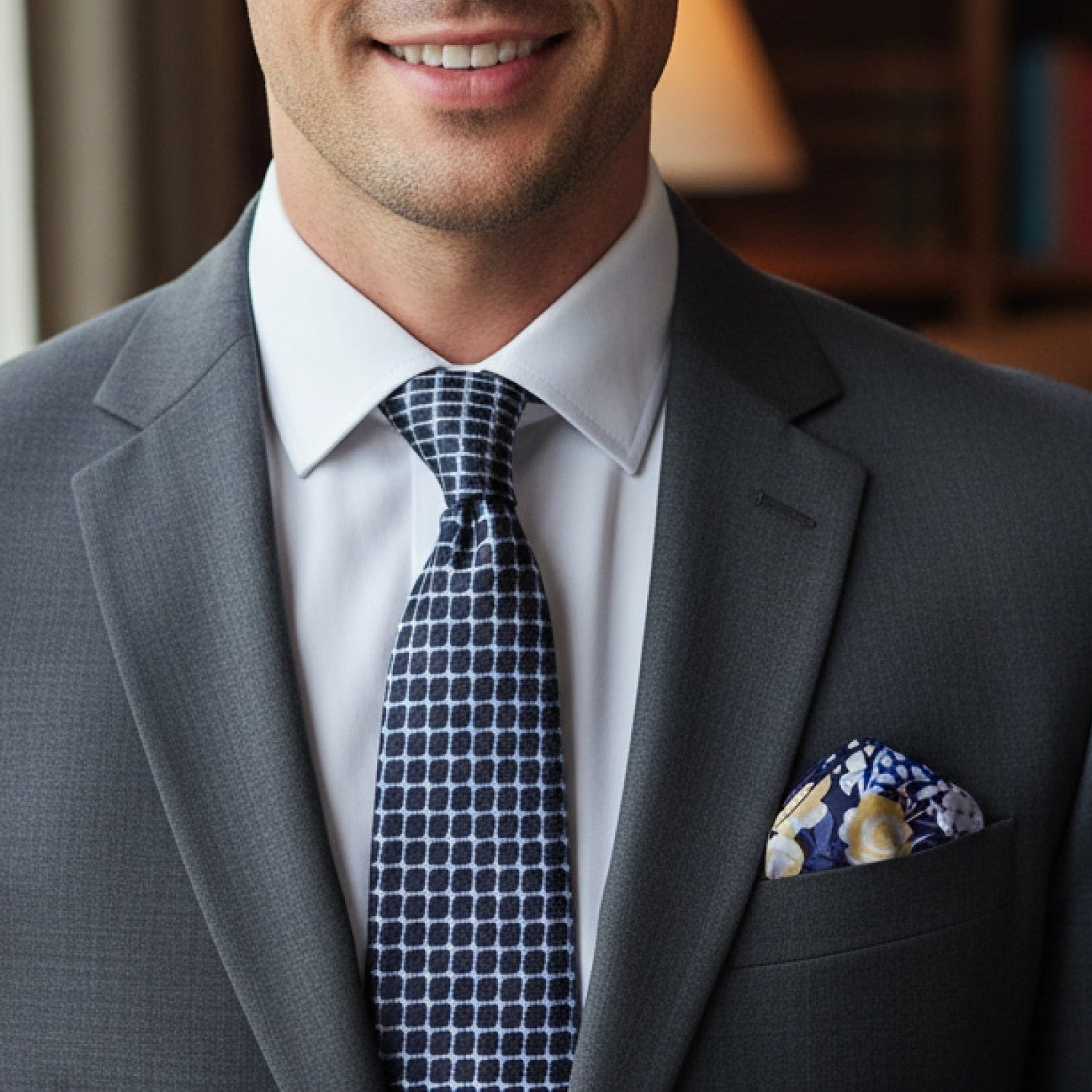 Man wearing a gray suit with a patterned tie and pocket square, smiling.