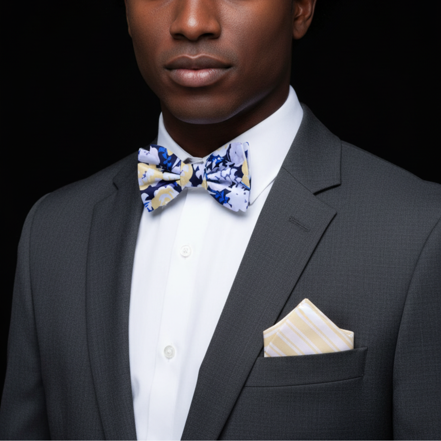 Man wearing a gray suit with a white shirt and colorful bow tie against a black background