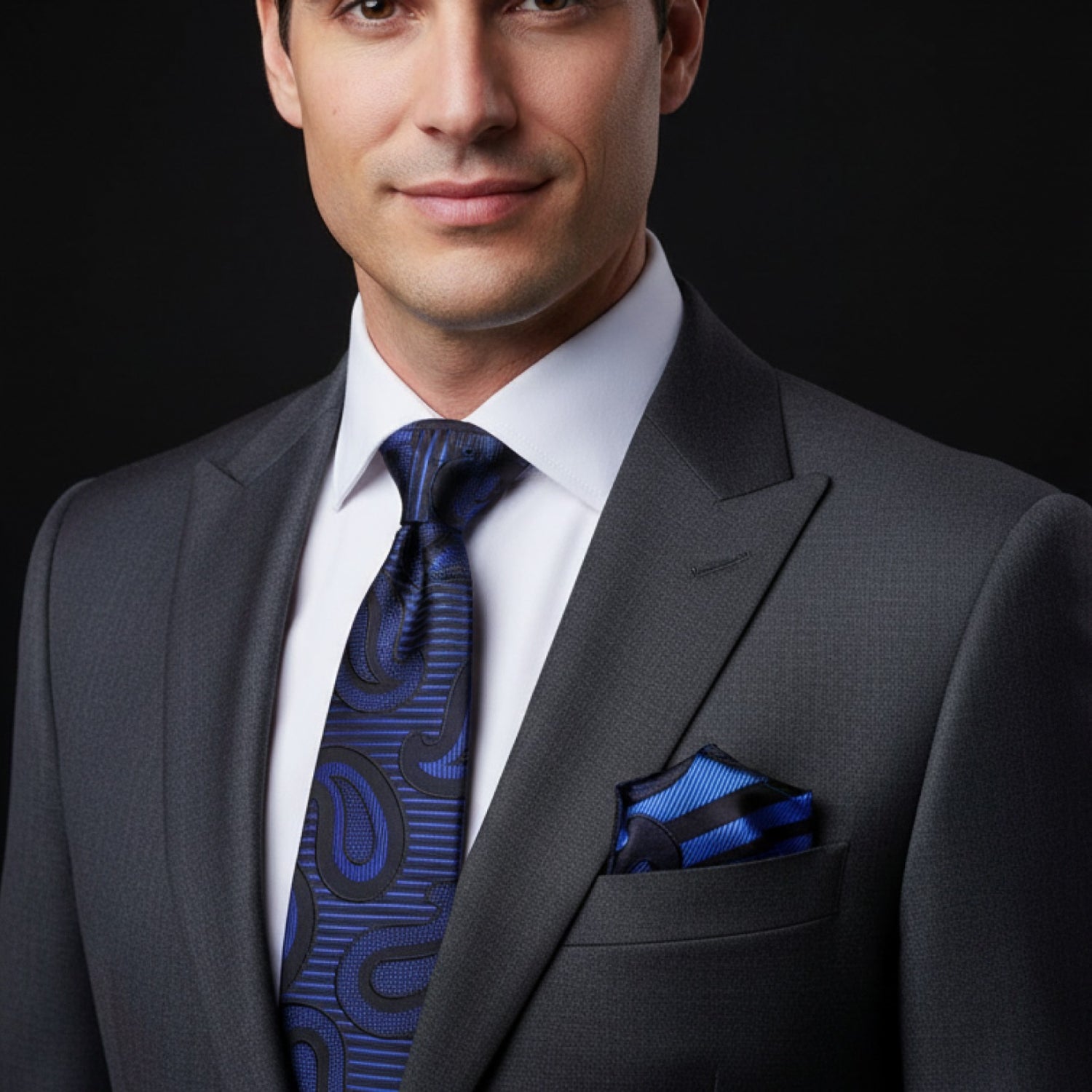Man wearing a gray suit with a blue tie and pocket square on a black background