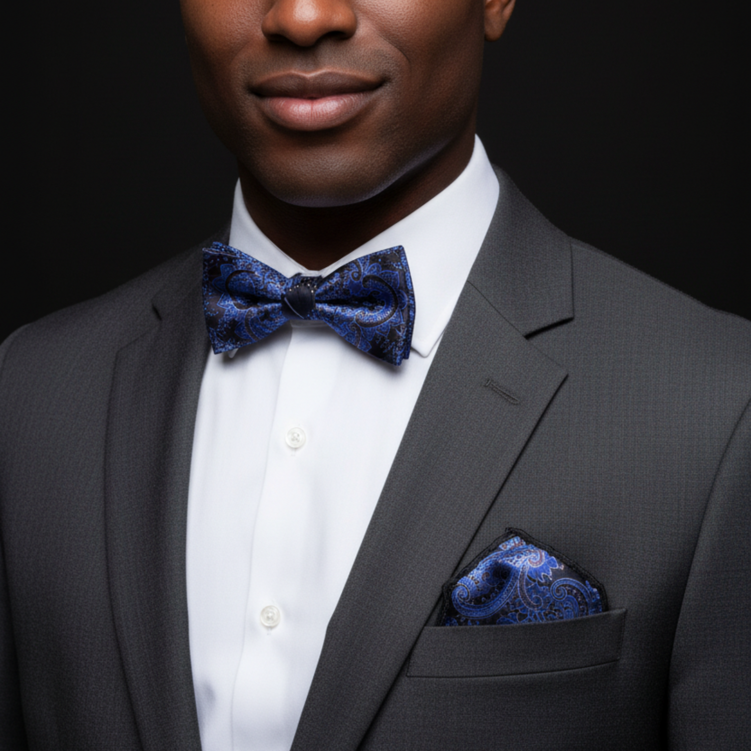 Man wearing a gray suit with a blue bow tie and pocket square against a black background