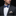 Man wearing a dark suit with a blue patterned bow tie and pocket square against a black background