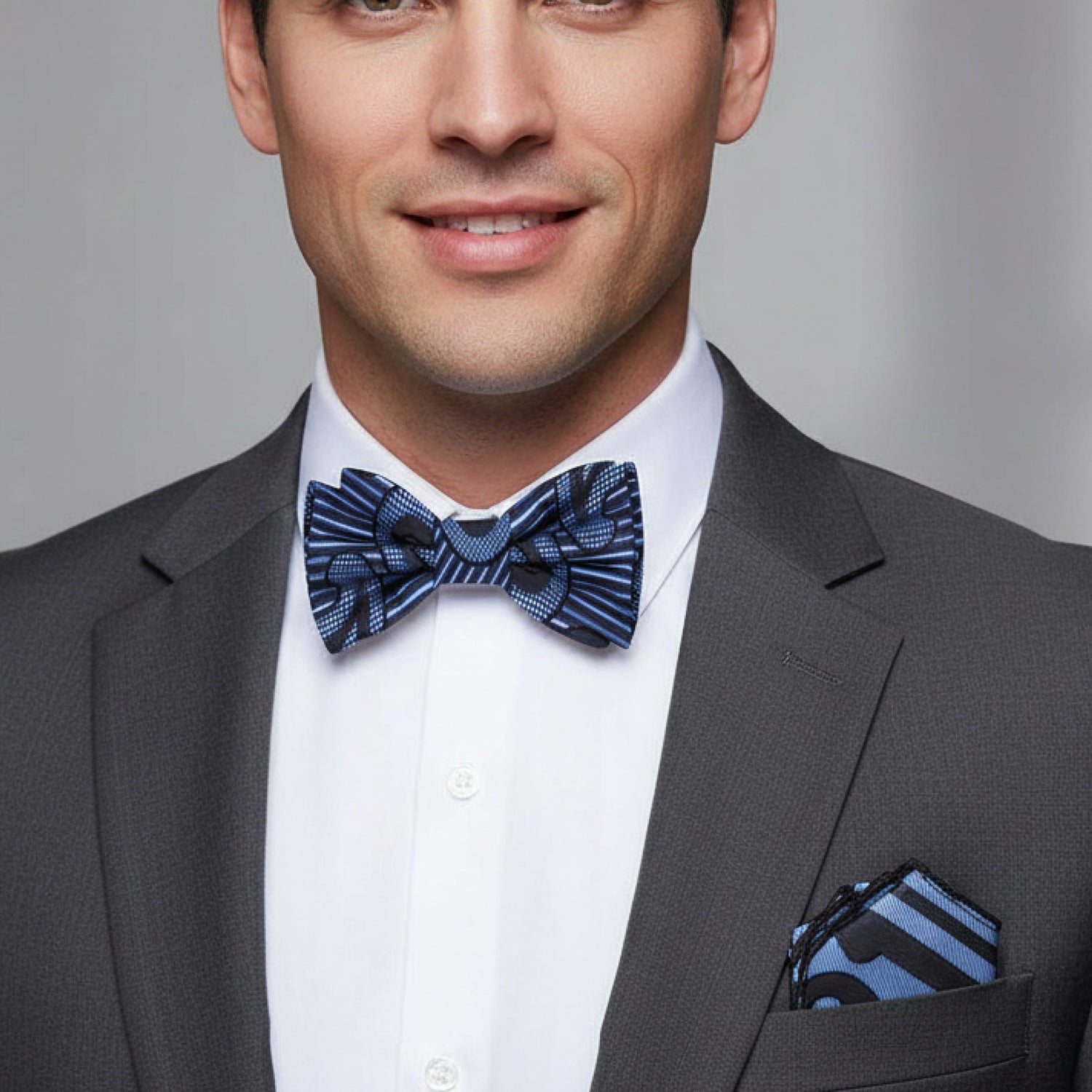 Man wearing a gray suit with a blue patterned bow tie and pocket square against a gray background