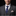 Man wearing a gray suit with a blue tie and patterned pocket square on a black background