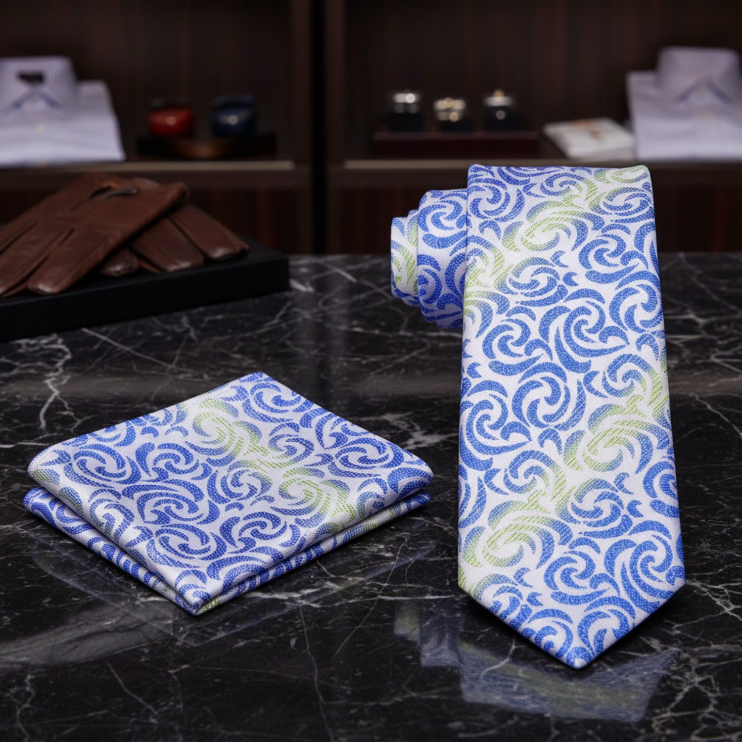Blue patterned tie and pocket square on a dark marble surface with blurred suits in the background