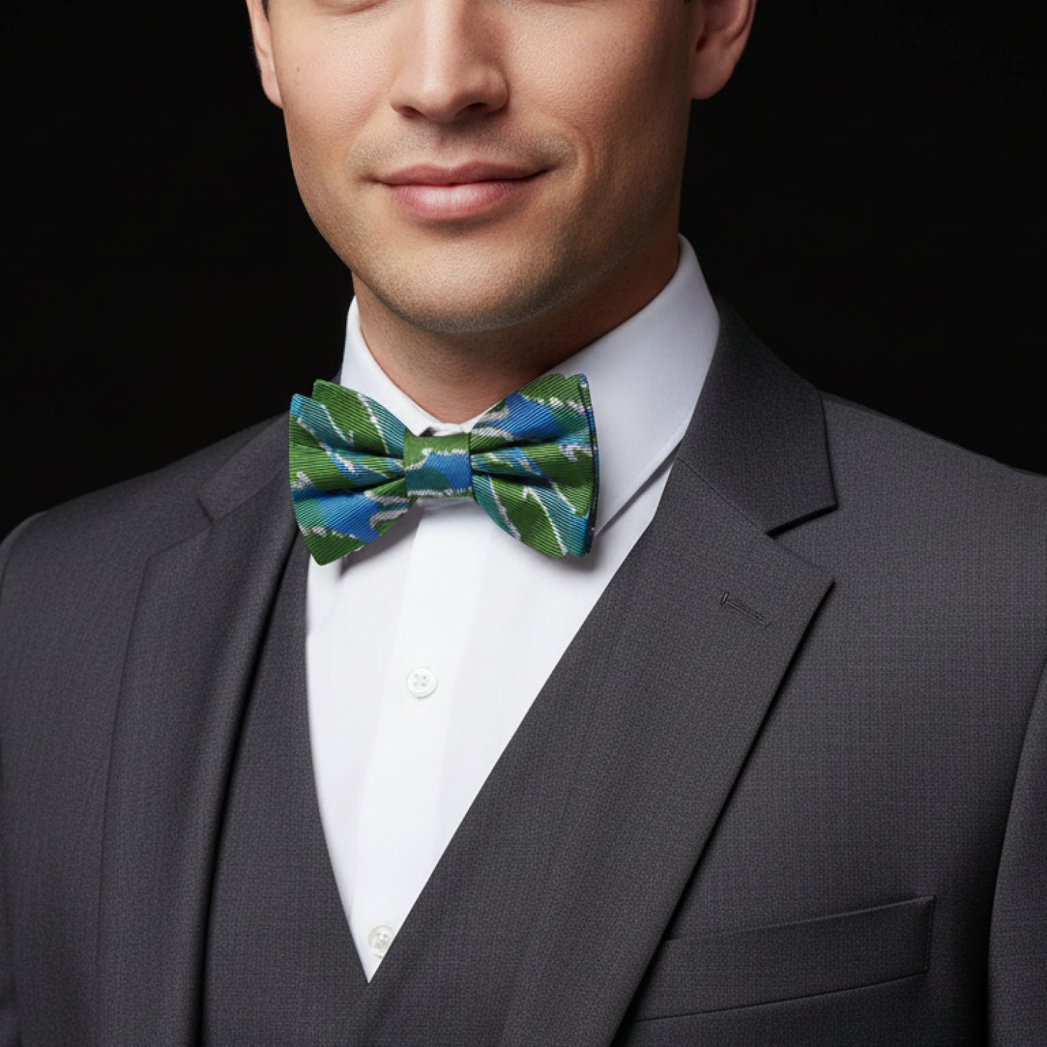 Man wearing a gray suit with a white shirt and a green patterned bow tie on a black background