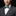 Man wearing a gray suit with a white shirt and a green patterned bow tie on a black background
