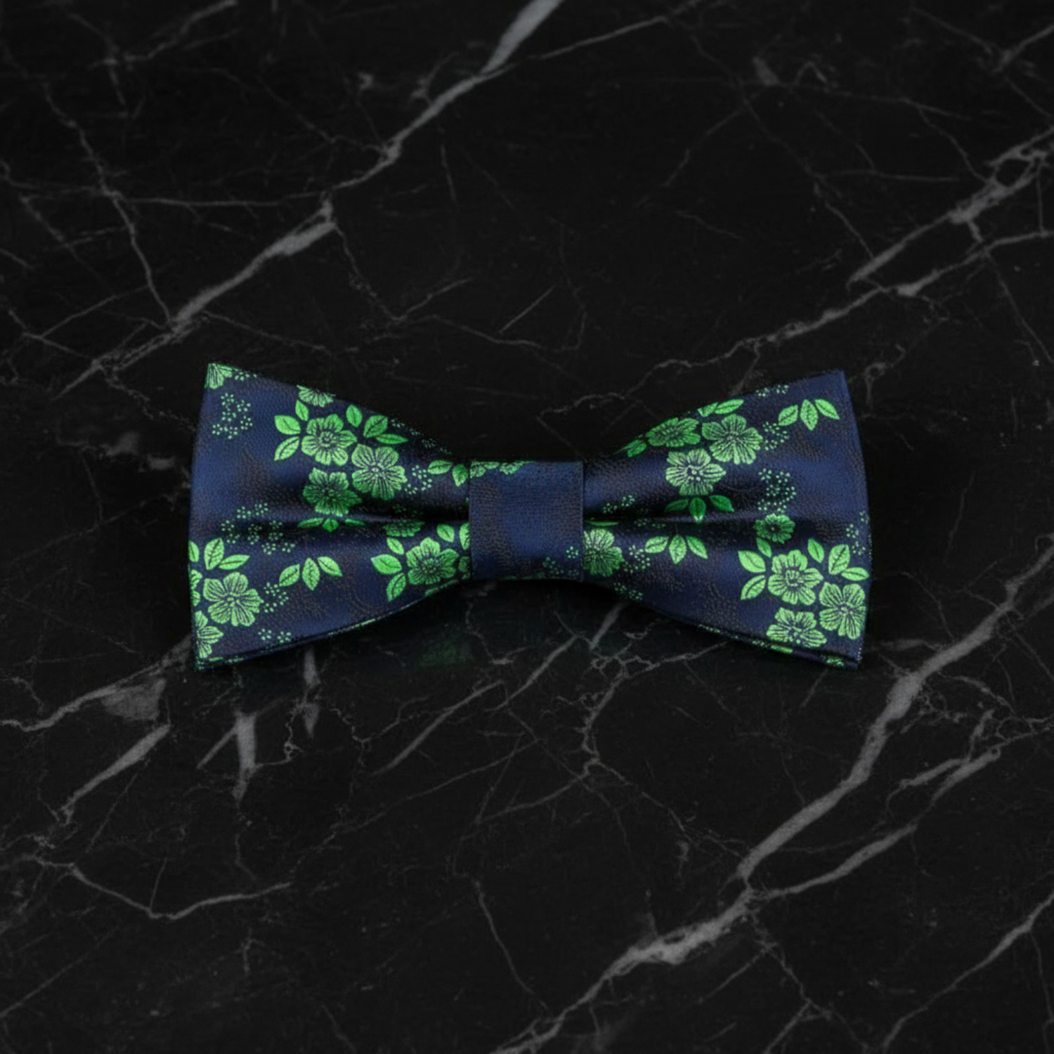 A dark blue silk bow tie with a green floral pattern laid out on a wooden surface.
