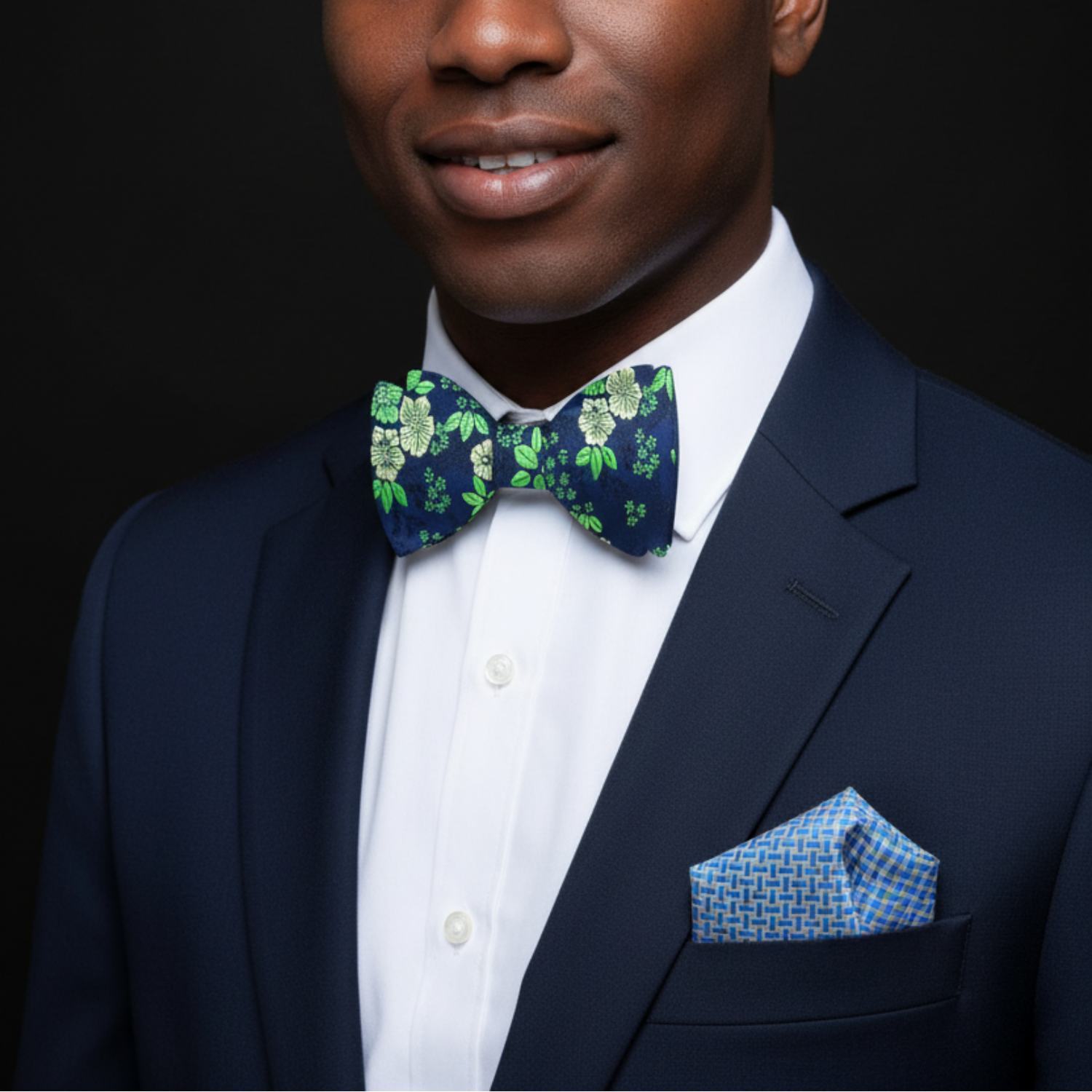 A dark blue silk bow tie with a green floral pattern laid out on a wooden surface.