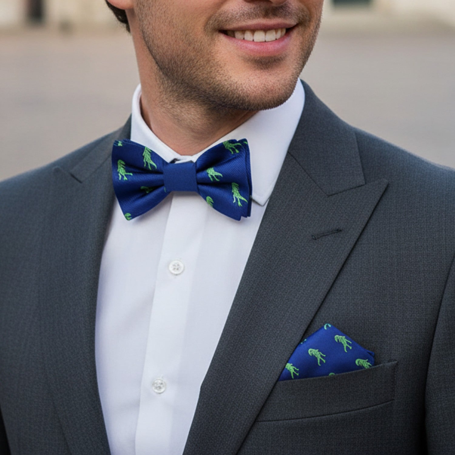 Man wearing a gray suit with a blue bow tie and matching pocket square, standing outdoors.