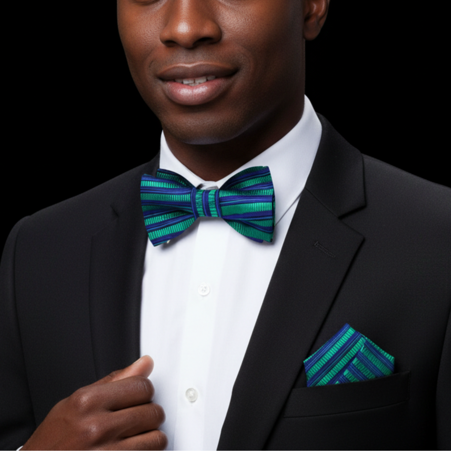 Man wearing a black suit with a green striped bow tie and pocket square on a black background