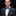 Man wearing a gray suit with a blue patterned bow tie and pocket square on a black background