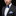 Man wearing a dark suit with a blue bow tie and pocket square on a black background