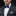 Man wearing a black suit with a blue bow tie and pocket square on a black background