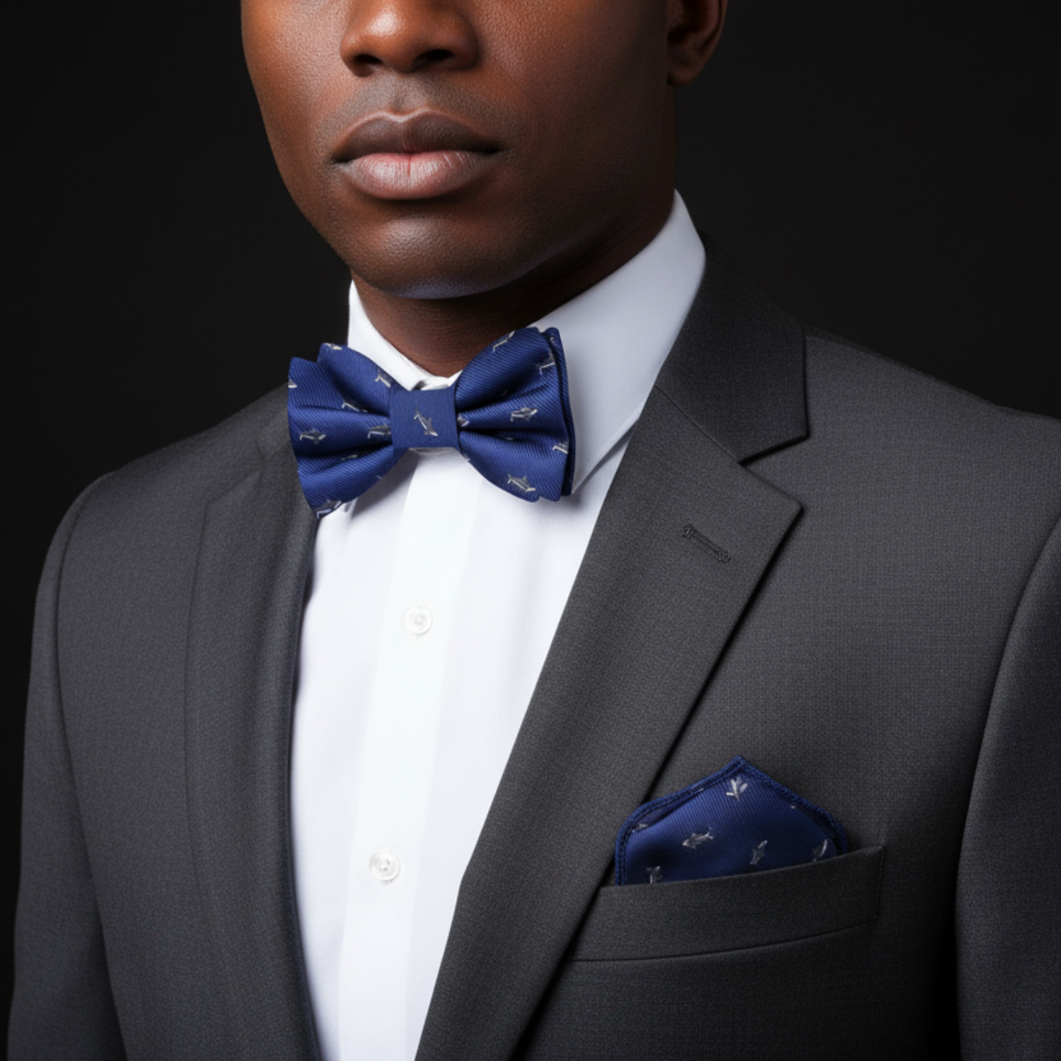 Man wearing a gray suit with a white shirt and blue bow tie and pocket square against a black background