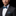 Man wearing a black suit with a blue plaid bow tie and pocket square against a black background