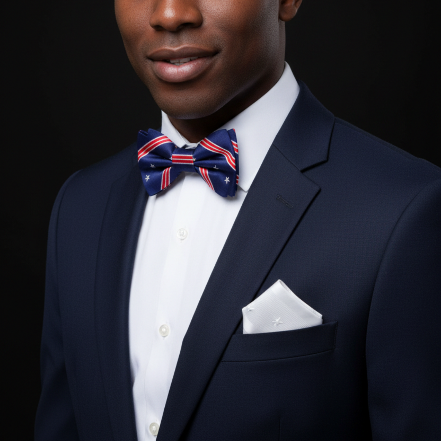 Man wearing a navy suit with a white shirt and red, white, and blue bow tie on a black background