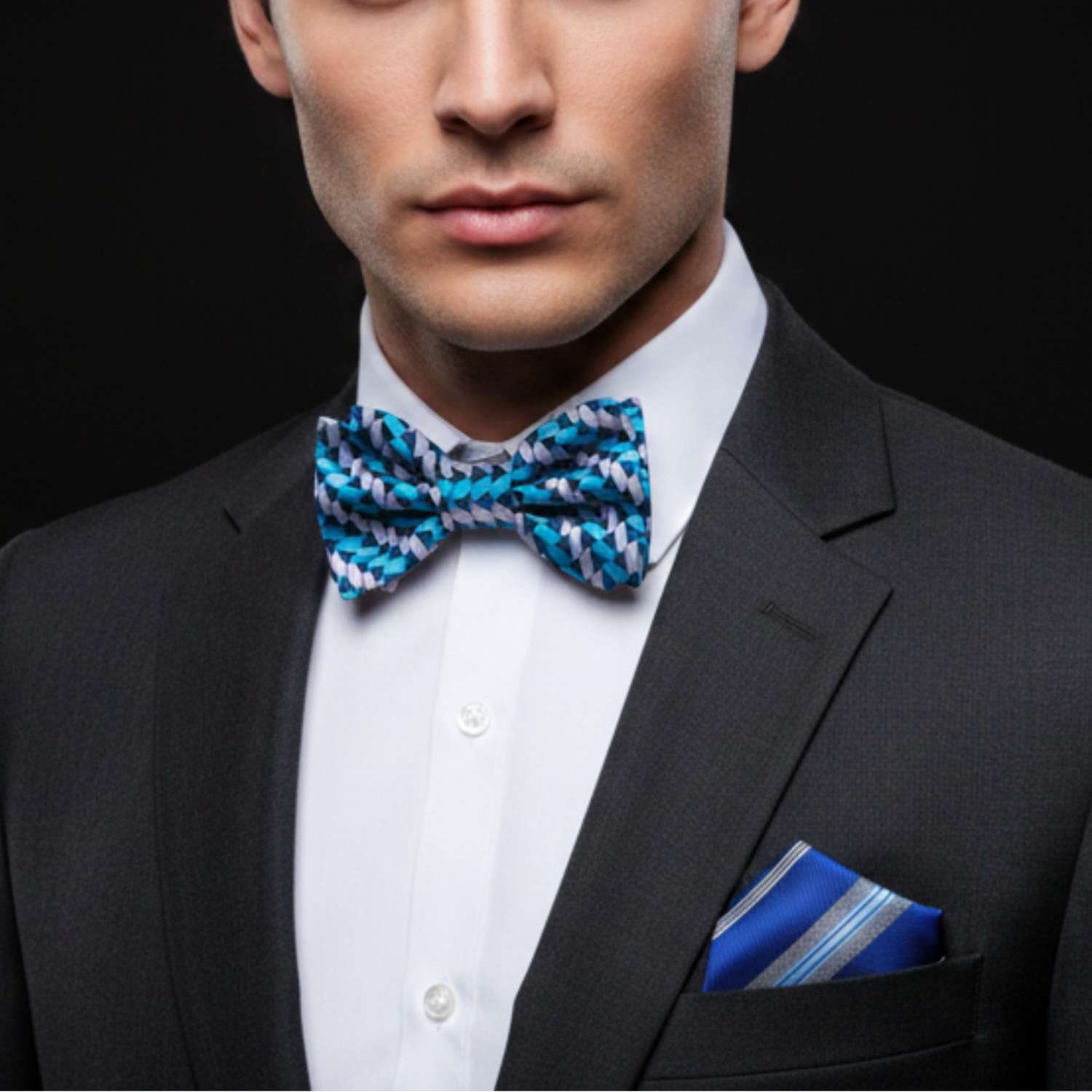 Man wearing a black suit with a blue and white patterned bow tie and pocket square on a black background