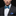 Man wearing a black suit with a blue and white patterned bow tie and pocket square on a black background