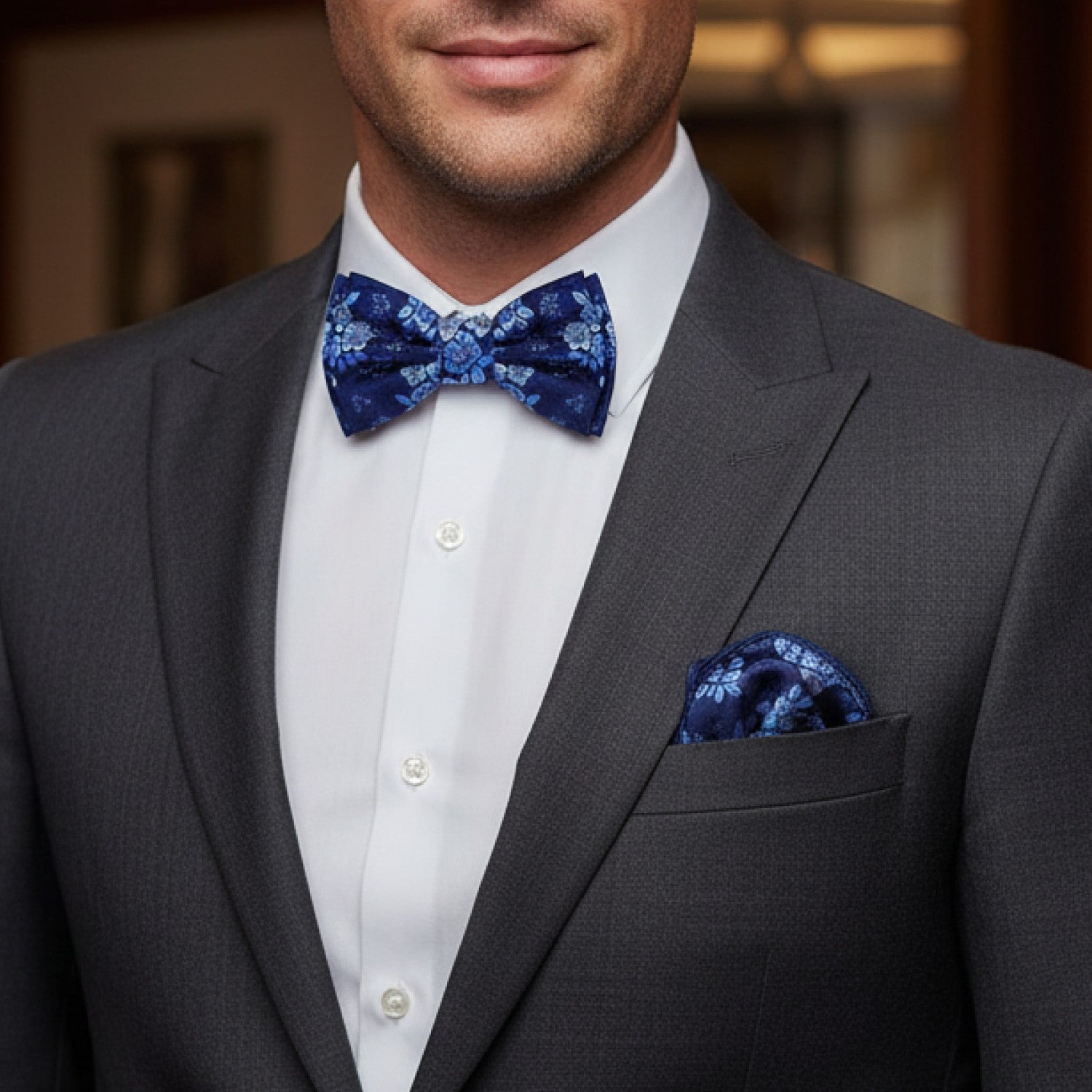 Man wearing a gray suit with a white shirt and blue floral bow tie and pocket square.