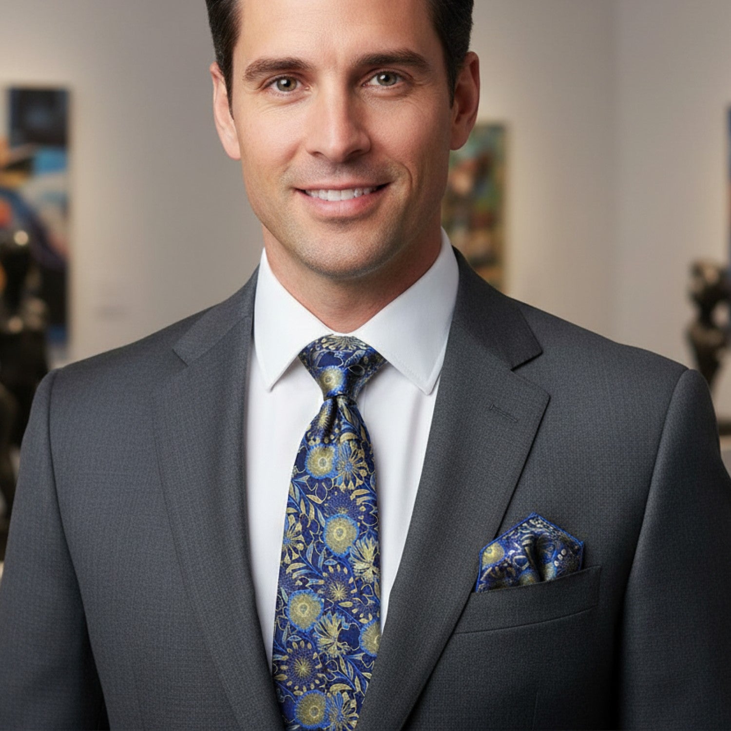 Man wearing a gray suit with a blue floral tie and pocket square, smiling.