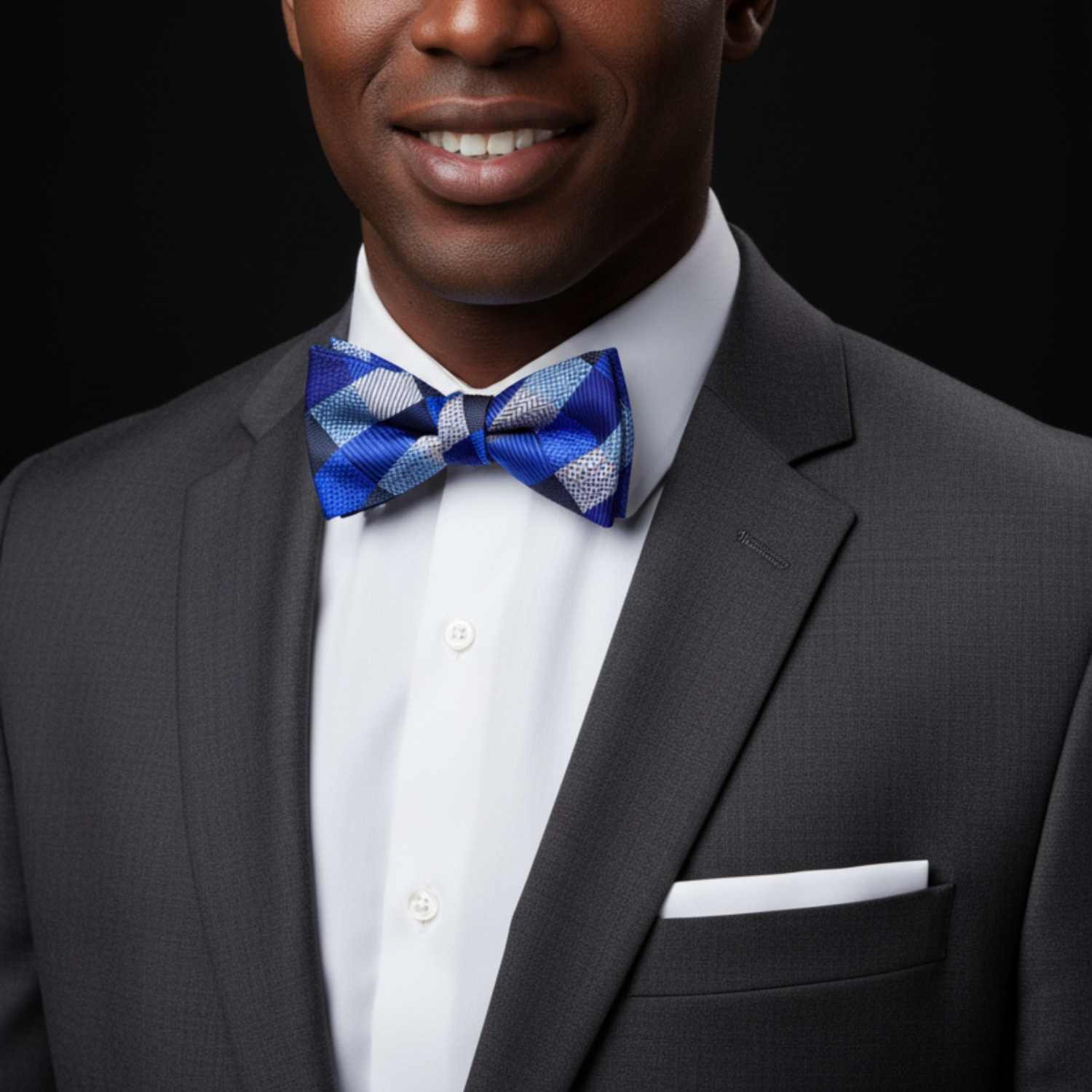 Man wearing a gray suit with a white shirt and blue bow tie on a black background
