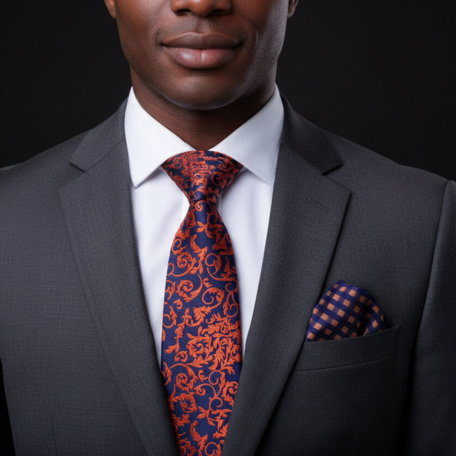 Man wearing a gray suit with a patterned red and blue tie and pocket square on a black background