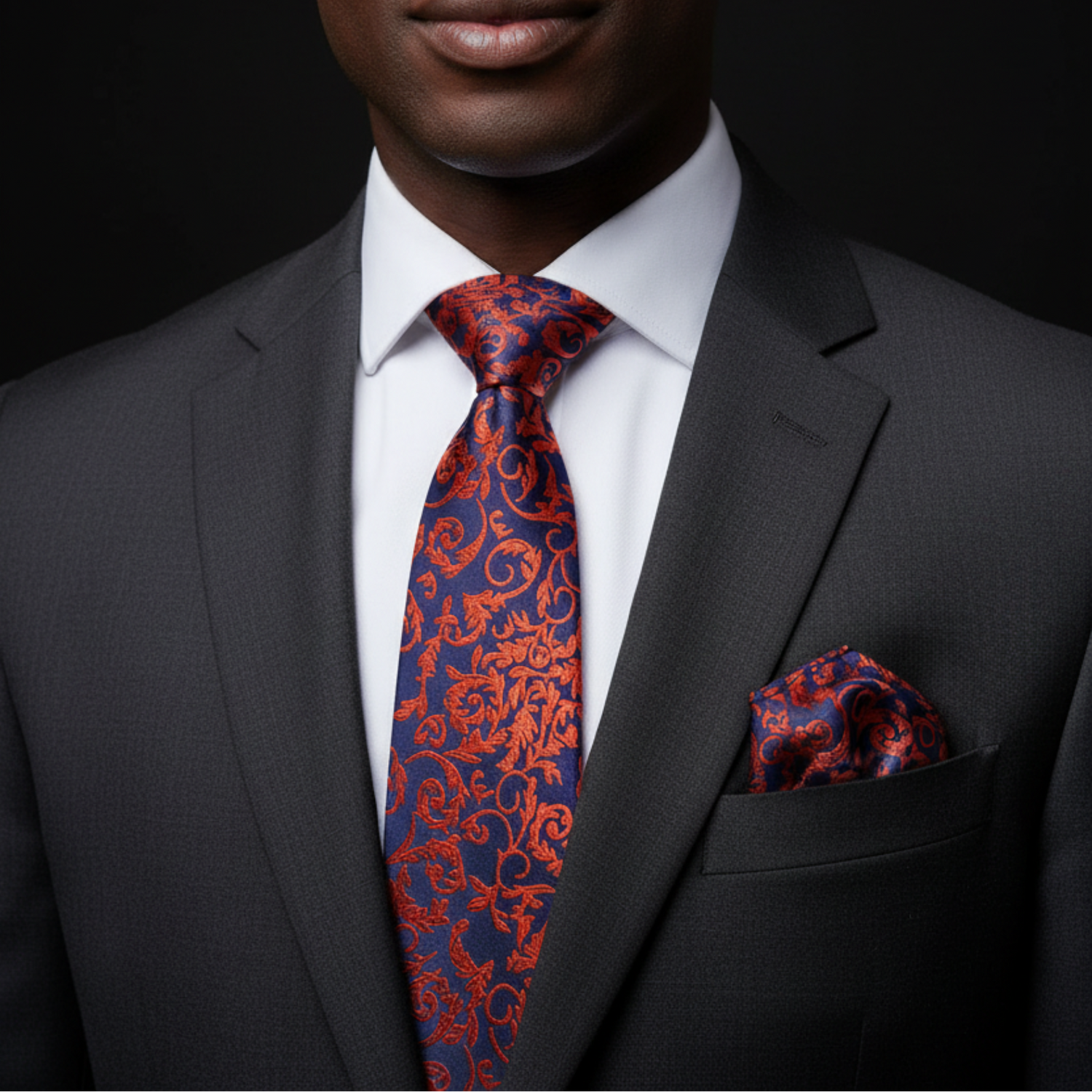 Man wearing a gray suit with a red and blue patterned tie and pocket square against a black background