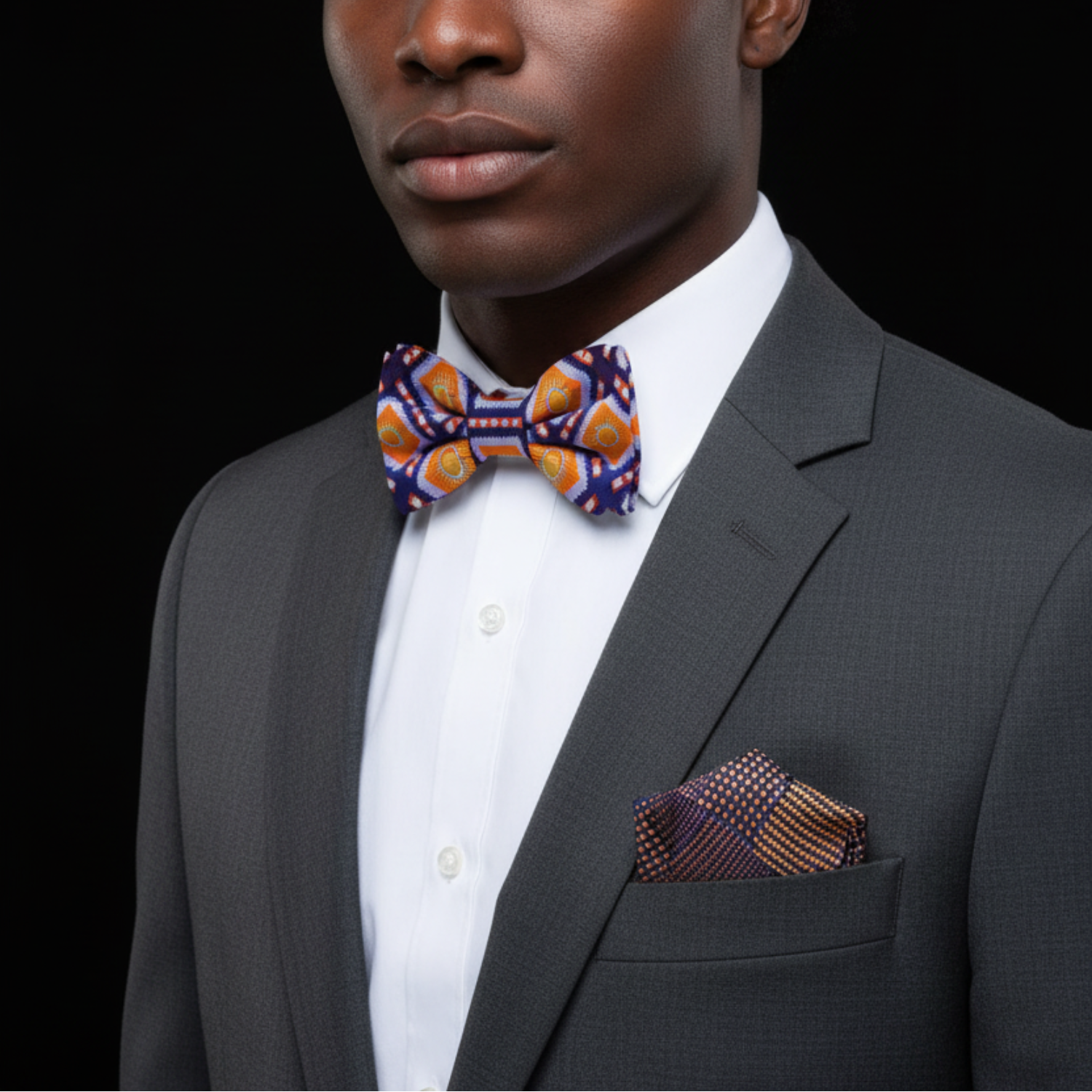 Man wearing a gray suit with a colorful bow tie and pocket square on a black background