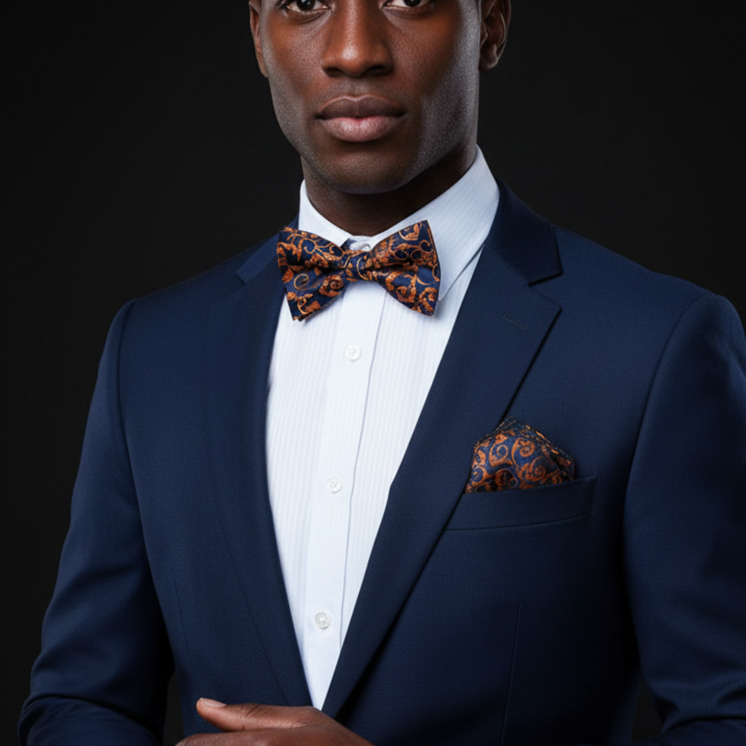 Man wearing a navy suit with a patterned bow tie and pocket square on a black background