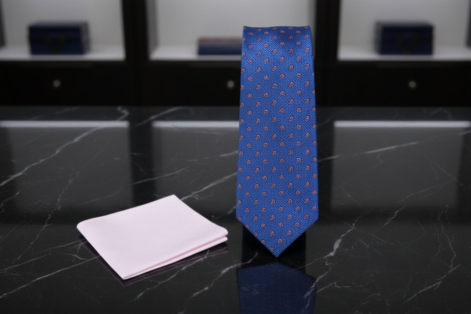 Blue patterned tie and soft pink pocket square on a white background