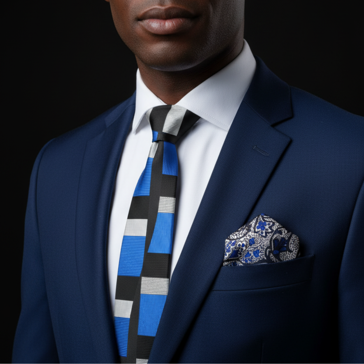 Man wearing a blue suit with a patterned tie and pocket square on a black background
