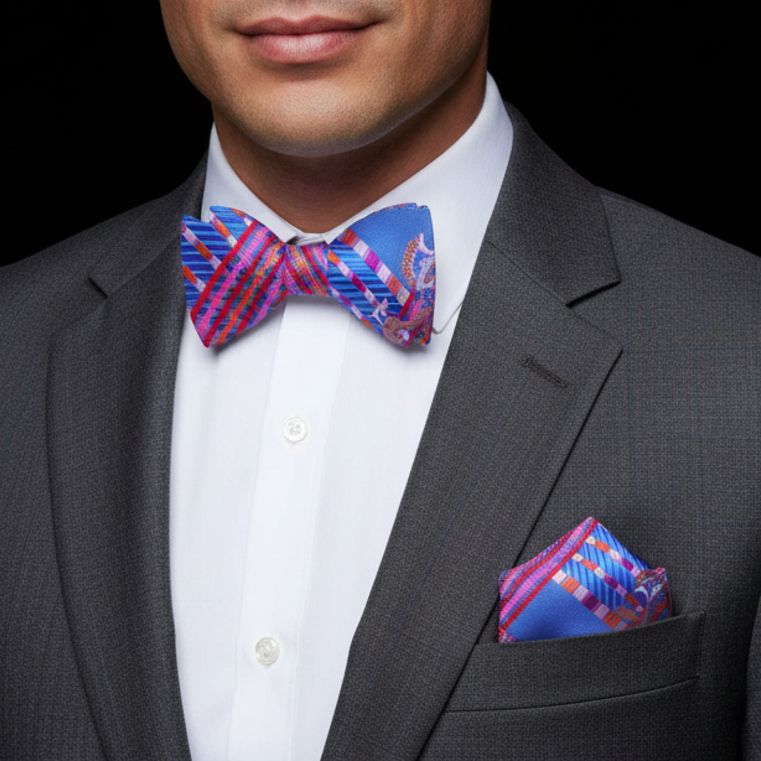 Man wearing a gray suit with a colorful bow tie and pocket square against a black background