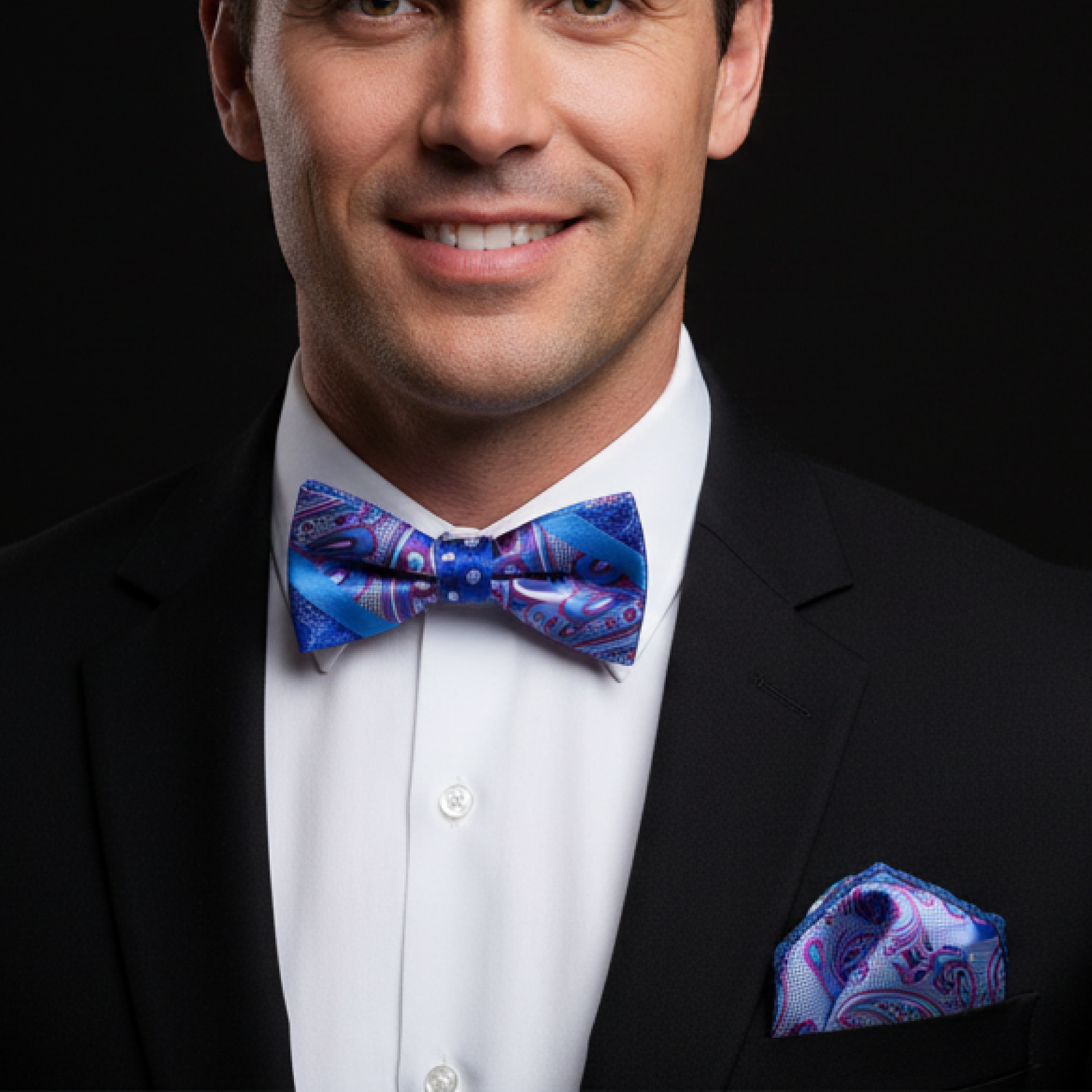 Man wearing a black suit with a blue bow tie and pocket square on a dark background
