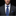 Man wearing a dark suit with a blue patterned tie and pocket square on a black background
